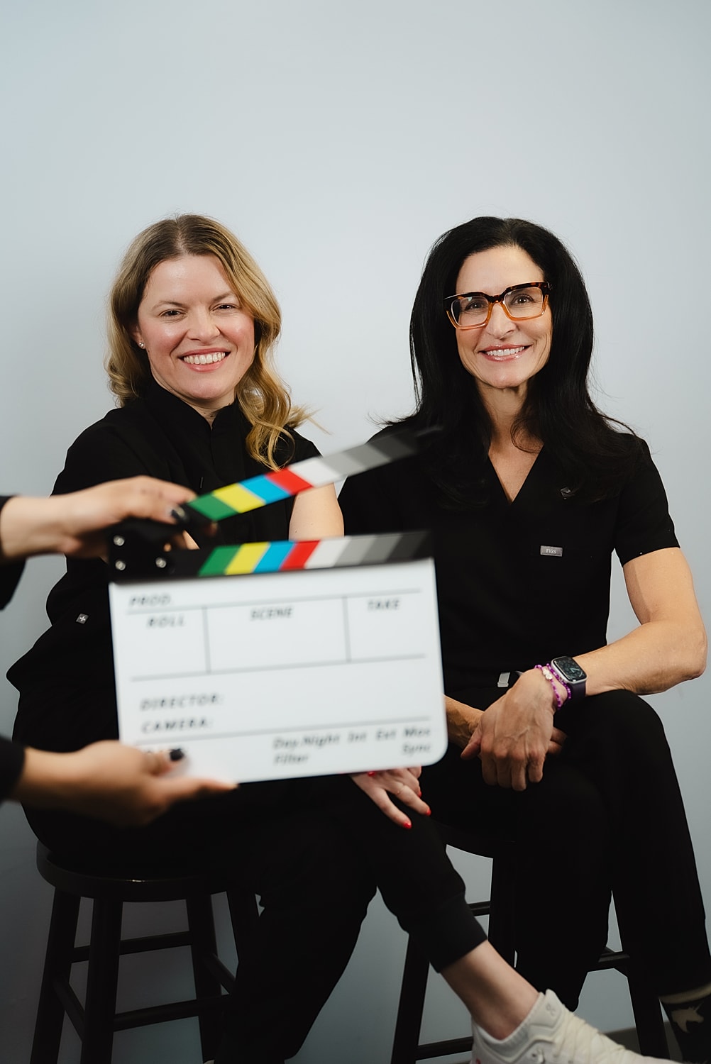 Two women posing with a movie clapperboard.
