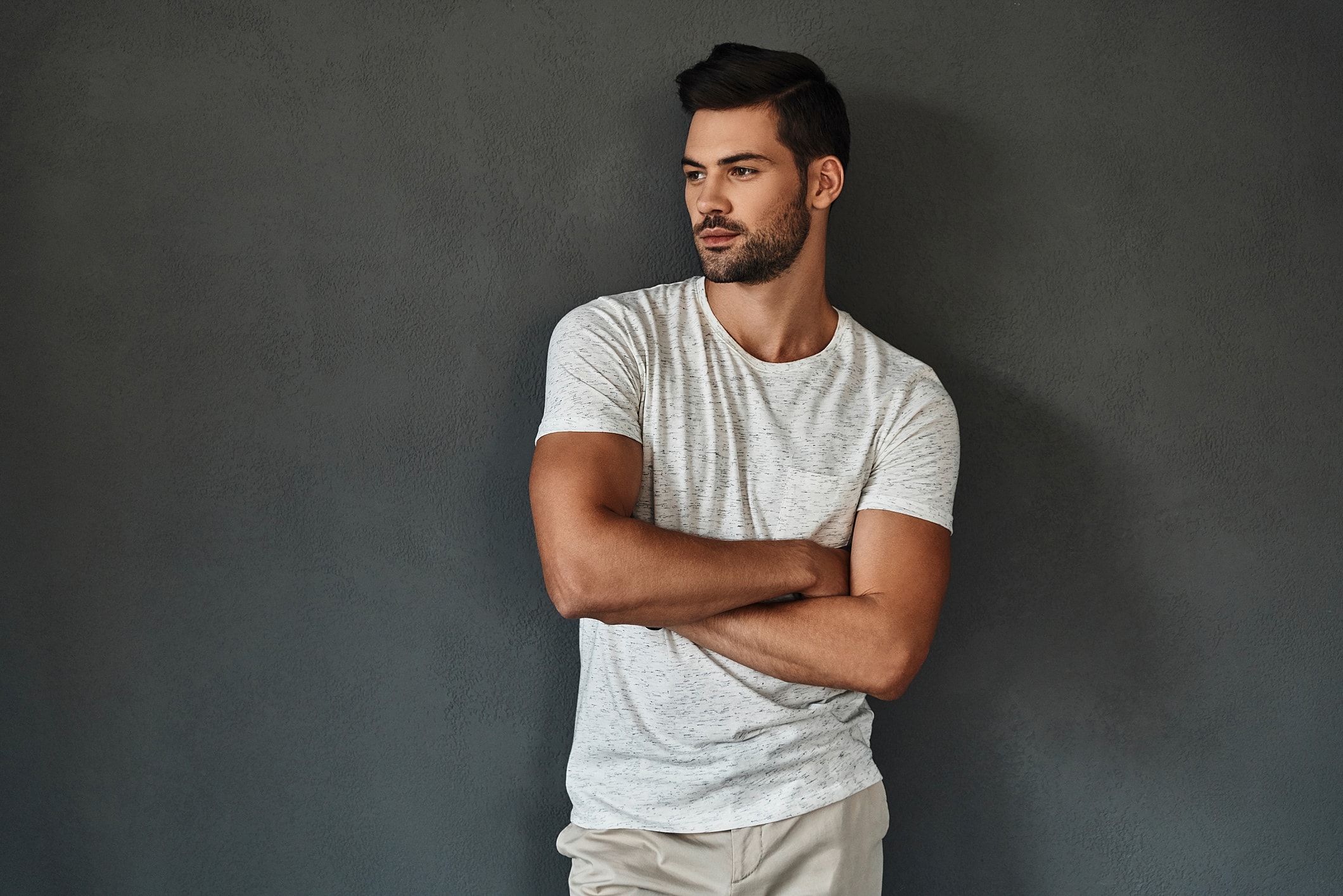 Man leaning against a dark wall, arms crossed.